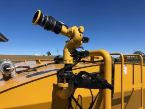 Close-up of a yellow firefighting nozzle mounted on top of a water tanker, under a clear blue sky. The nozzle is designed for precision and flexibility in directing water flow.